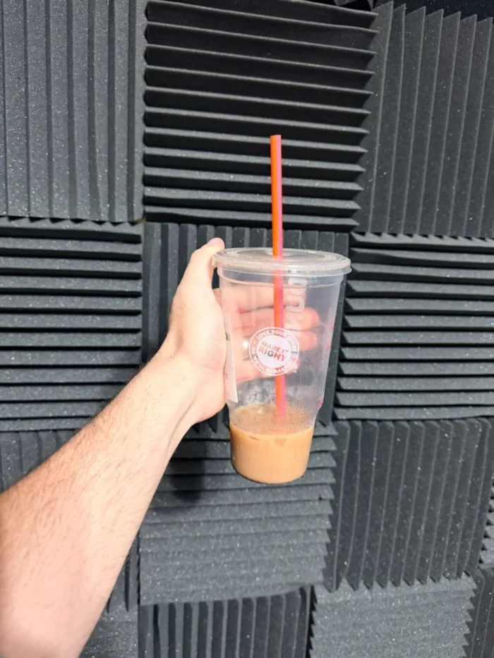 A hand holding up an iced coffee with a pink straw